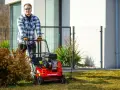 Mężczyzna używa wertykulatora, aby przygotować trawnik do wiosny. Urządzenie to służy do usuwania mchu i filcu z trawnika.